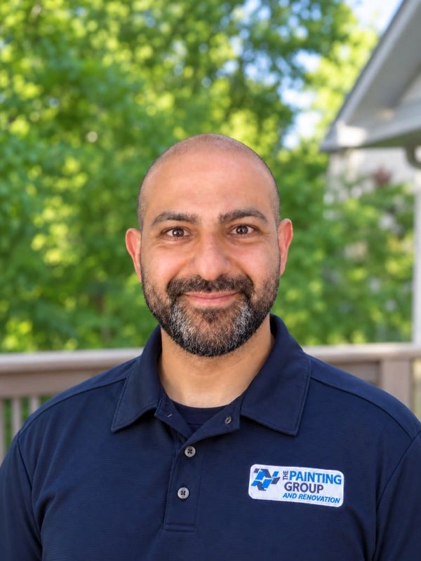 Masom smiling outdoors in a navy company polo, with trees behind him