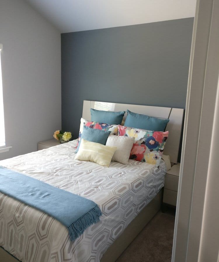 Bedroom with a gray accent wall behind a bed with colorful pillows