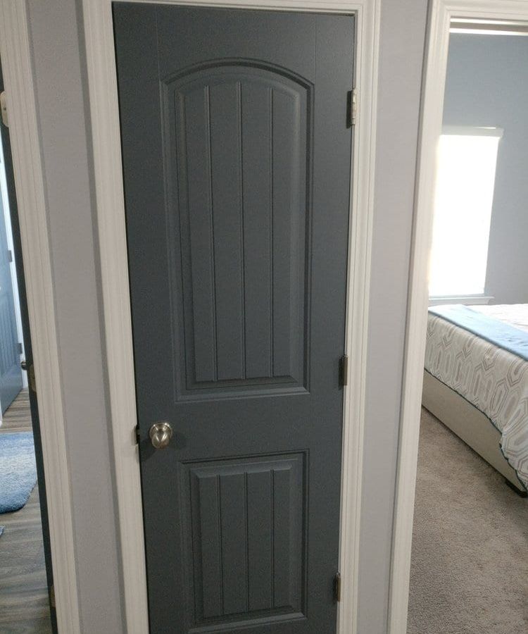 Charcoal gray paneled door beside a doorway into a bedroom
