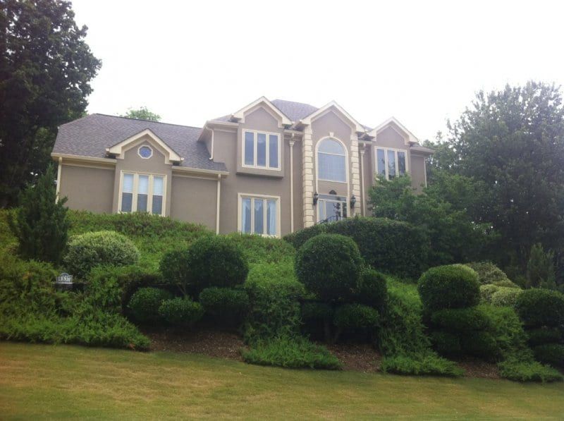 Beige stucco two-story house on a hill above rounded shrubs