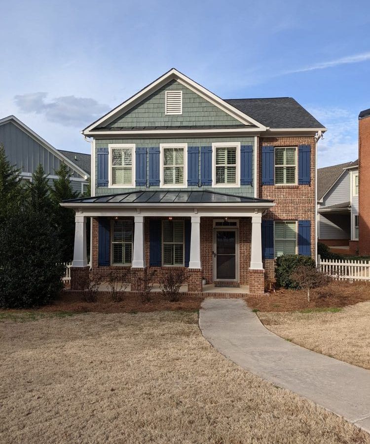 Two-story brick house with blue-gray siding and shutters, a front porch, and a walkway