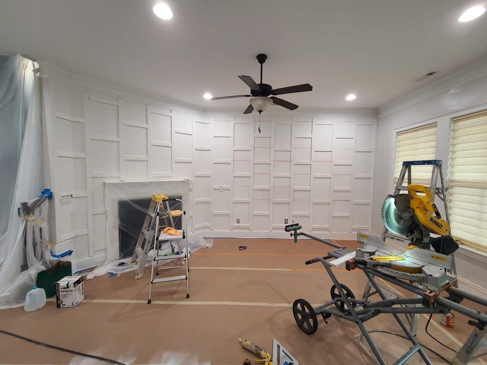 Living room being prepped, with a white box-molding wall, a miter saw and drop cloths