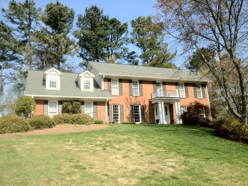 Brick and white sided two-story house above a long front lawn