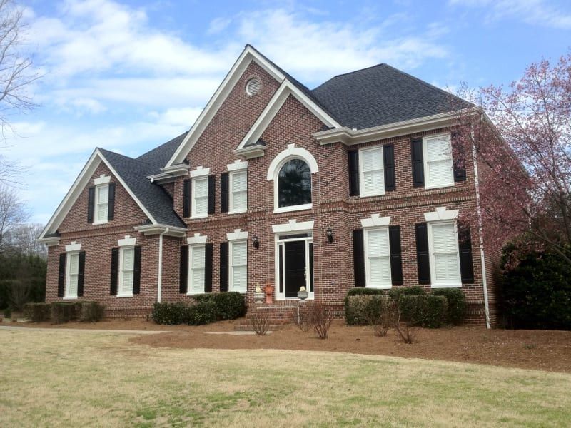 Red brick two-story colonial with an arched front window and black shutters