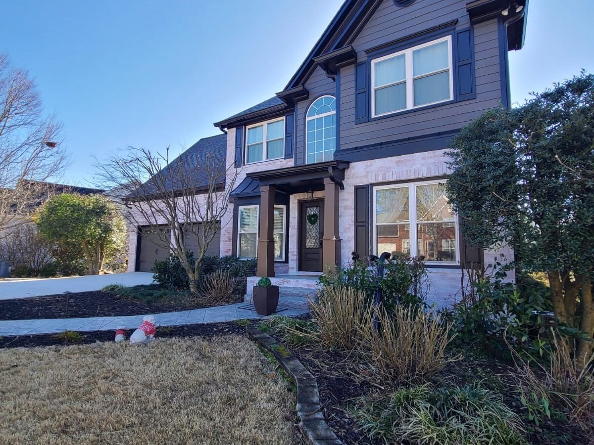 Front of the charcoal gray house, with a covered entry and landscaped beds