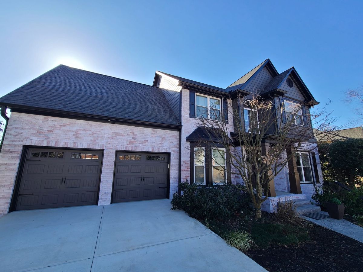 Charcoal gray two-story house with whitewashed brick, dark garage doors, and a covered front entry
