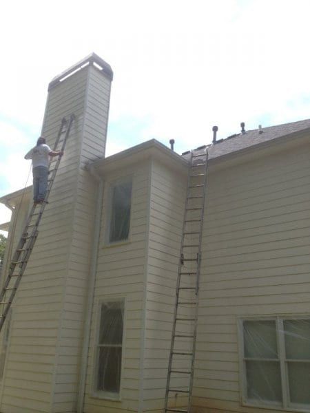 Painter on a ladder at the top of a chimney on a cream sided house