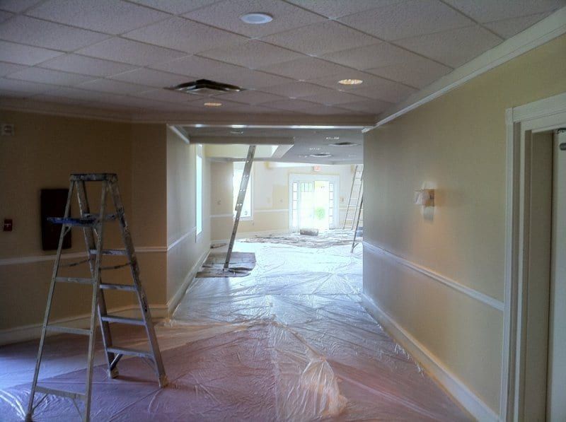 Church hallway with a drop ceiling, a ladder, and covered floors
