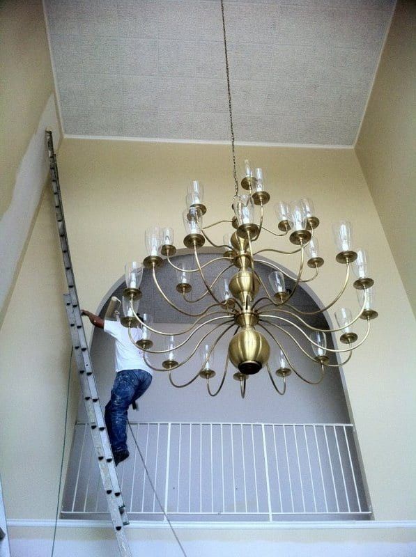 Painter on a ladder beside a brass chandelier in the foyer