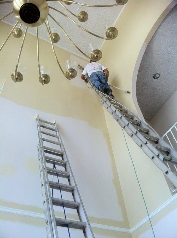 Painter high on a ladder next to the foyer chandelier