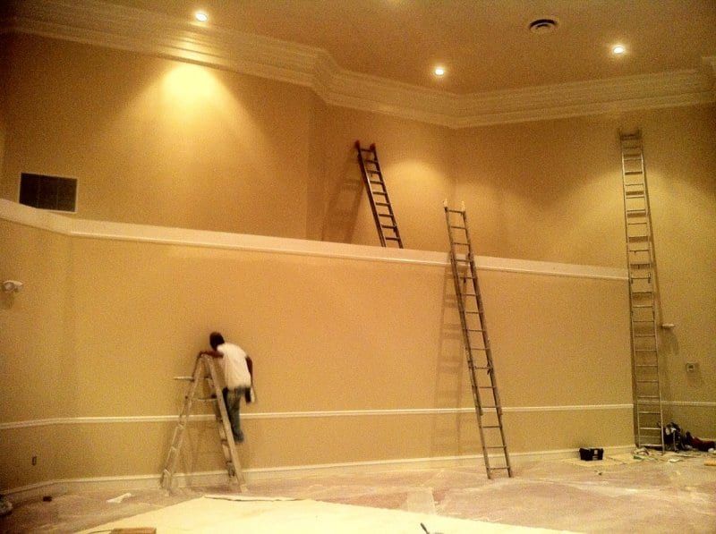 Painters on ladders along a long sanctuary wall with crown molding