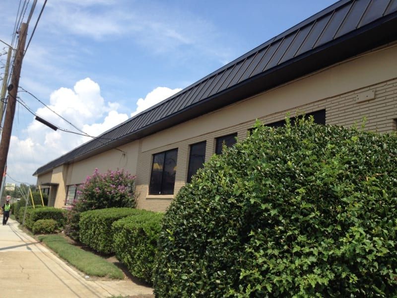 Low commercial building with a dark metal roof behind hedges