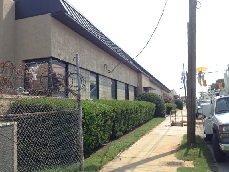 Commercial building with a metal roof and large windows behind a chain-link fence