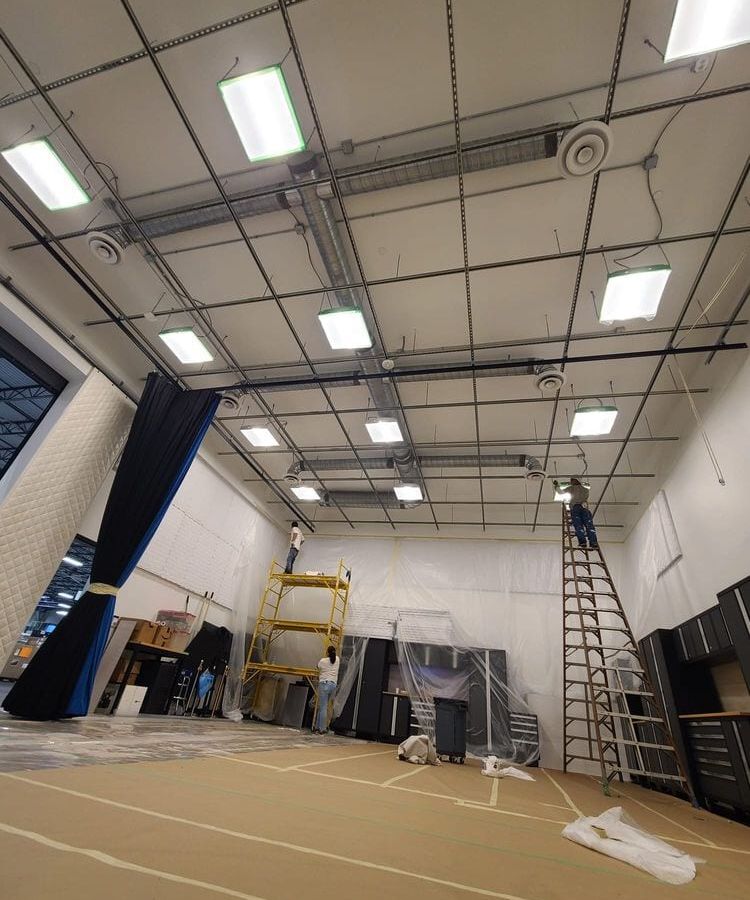 Large commercial room with a drop-ceiling grid, ladders, and the floor covered in paper