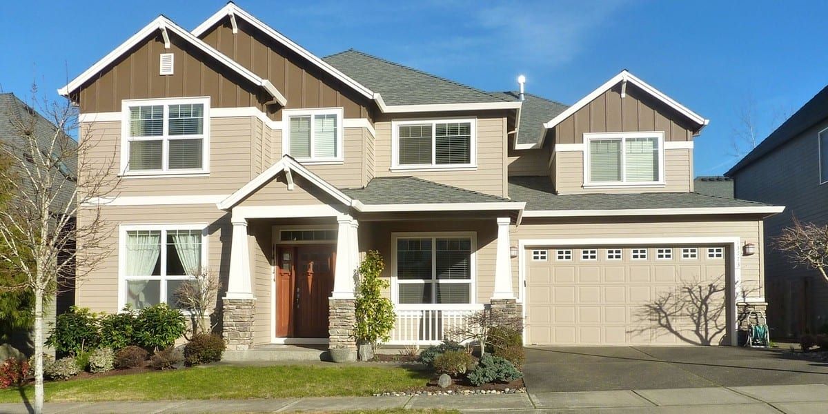 Two-story craftsman house with tan siding, brown board-and-batten gables, and white trim