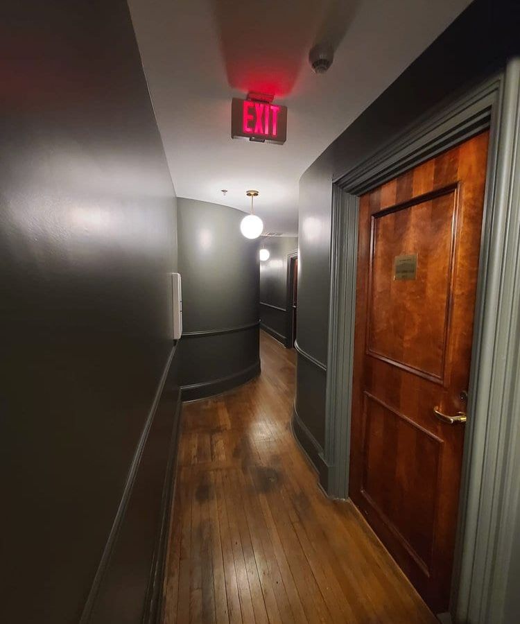 Hallway with dark painted walls, wood doors, and an exit sign overhead