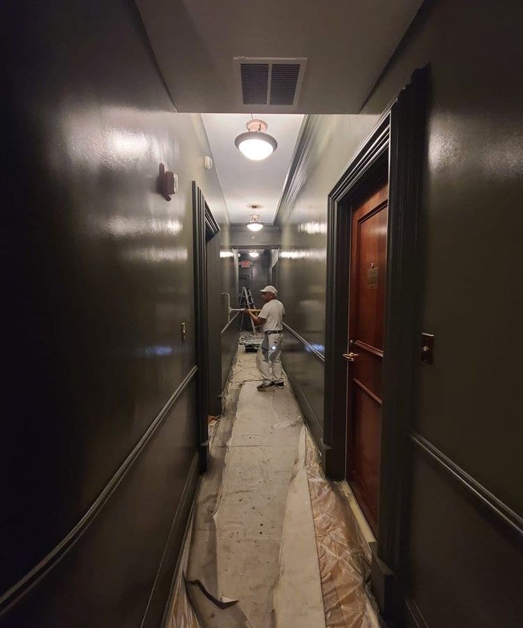 Dark hallway with drop cloths on the floor and a painter at work far down the hall