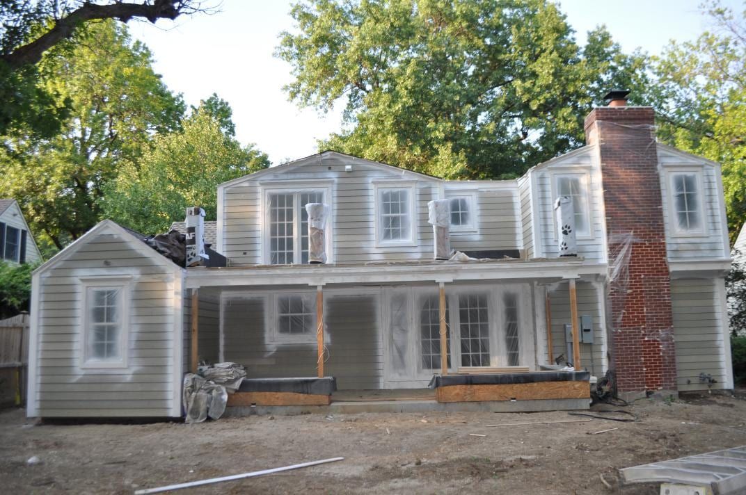 Older two-story house during exterior prep, with bare siding and a brick chimney