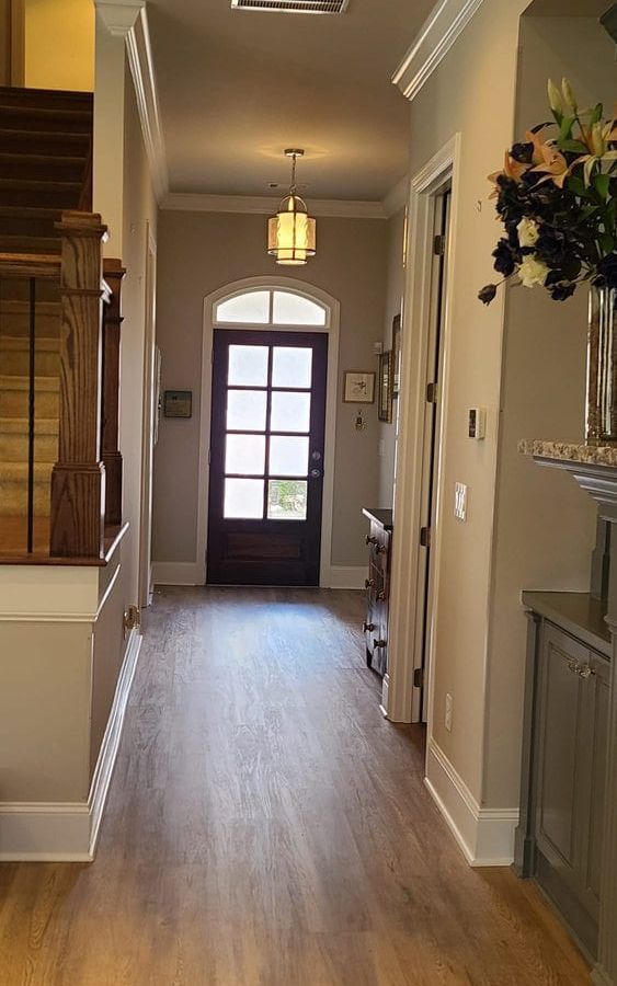 Hallway with hardwood floors leading to a glass front door under a hanging light