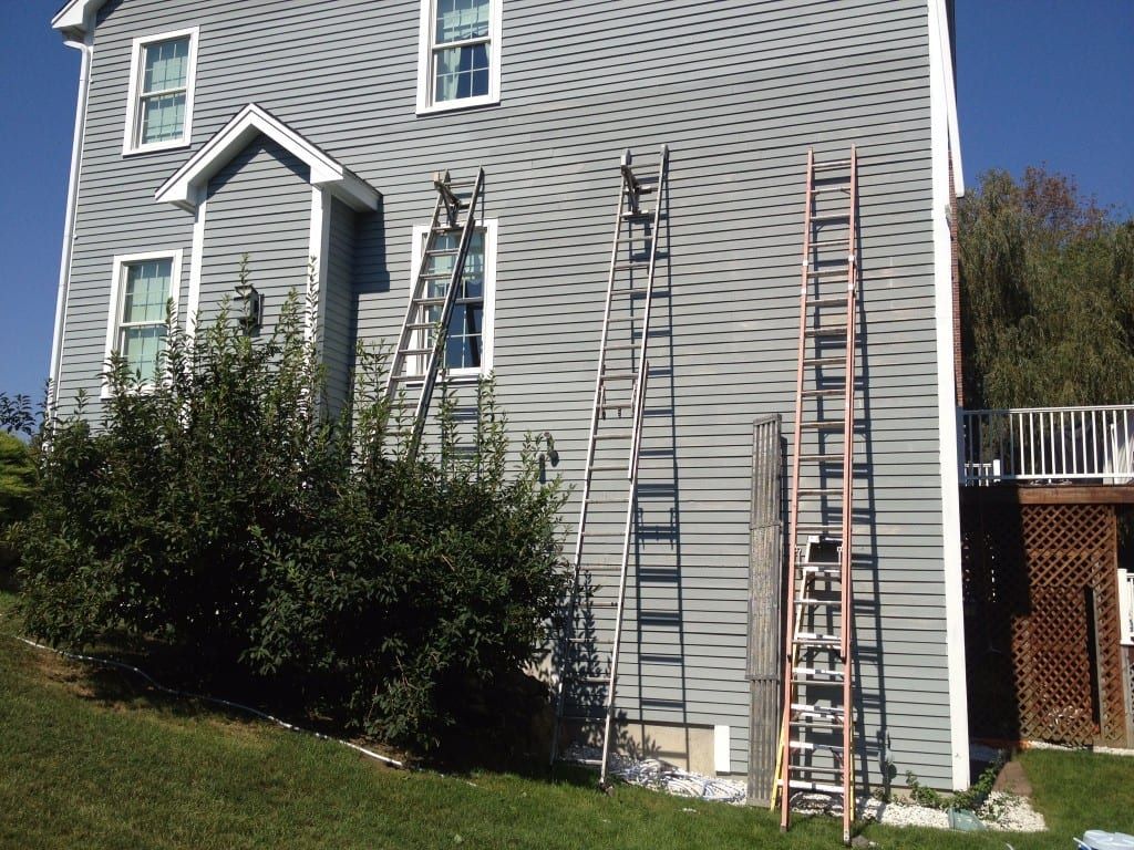 Gray sided house with tall ladders set against the wall