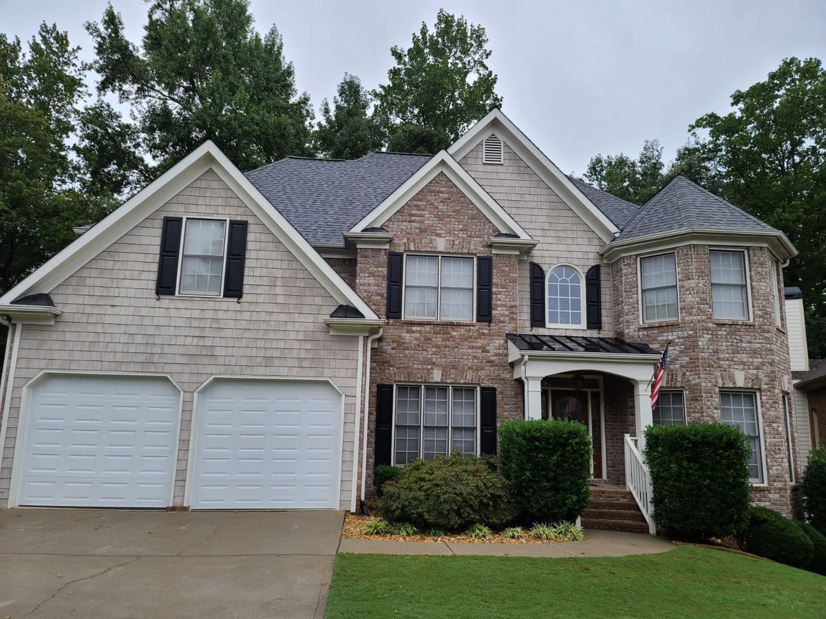 Two-story house with brown cedar shingles, brick, and black shutters