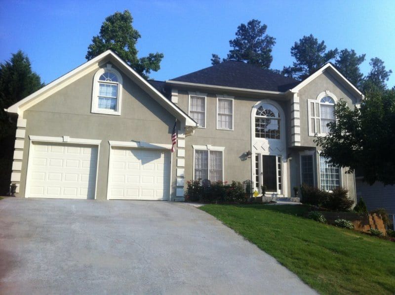 Gray stucco two-story house with white trim, arched windows, and two garage doors