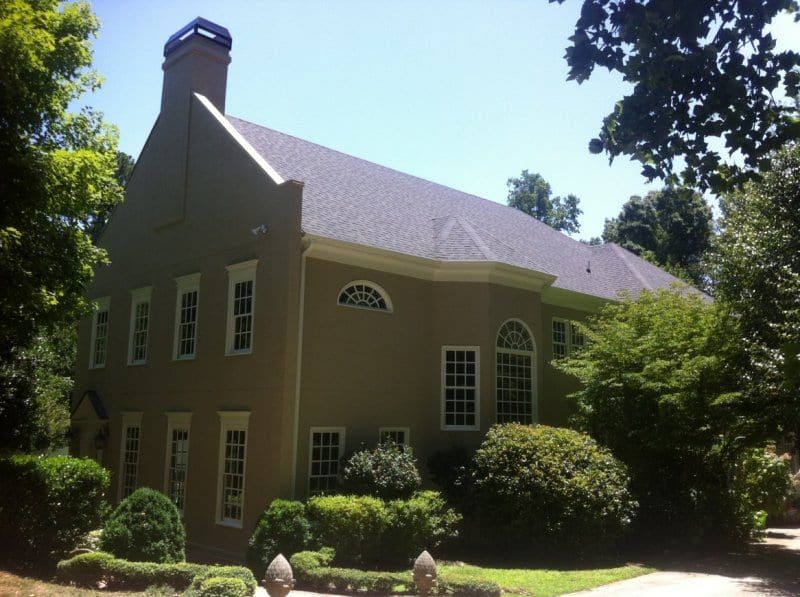 Gray stucco house with white windows and a steep roof