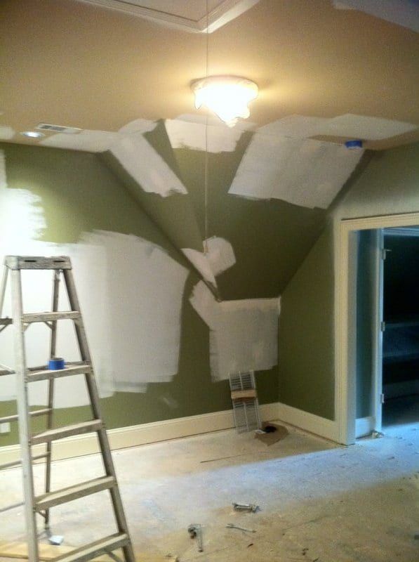Living room mid-project, with a ladder, a covered floor, and fresh primer patches on the walls