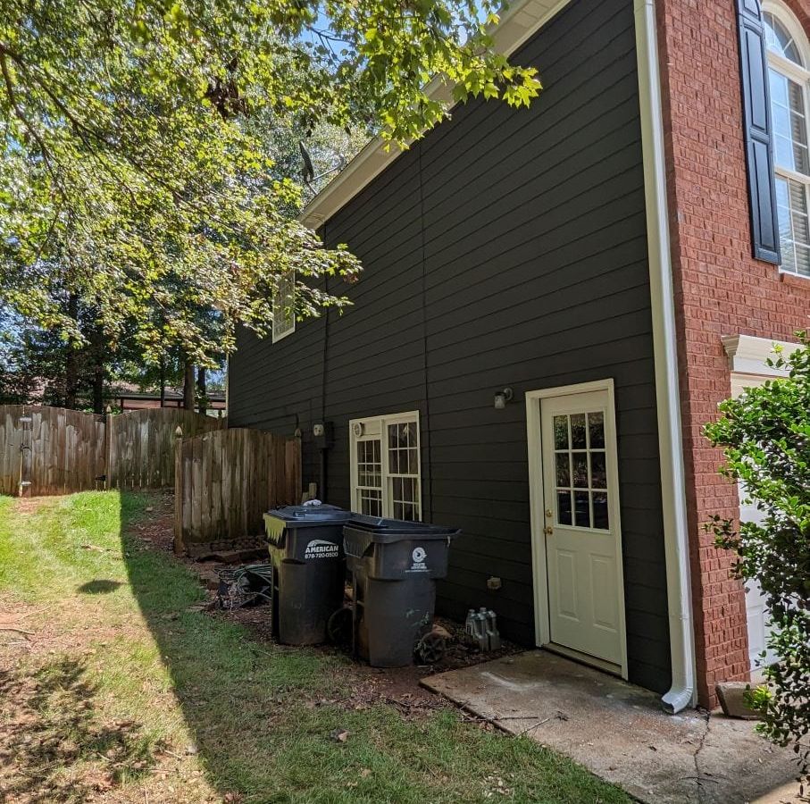 Side of a navy sided house with a white door and a red brick corner