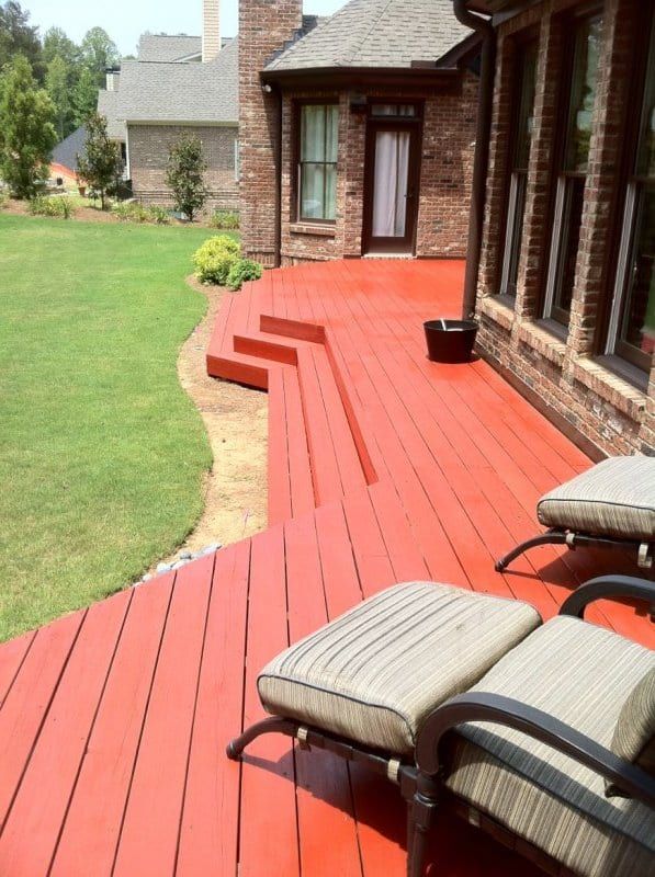Red-stained deck with lounge chairs beside a brick house