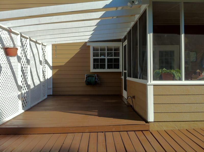 Stained wood deck under a screened porch, with tan siding and white trim