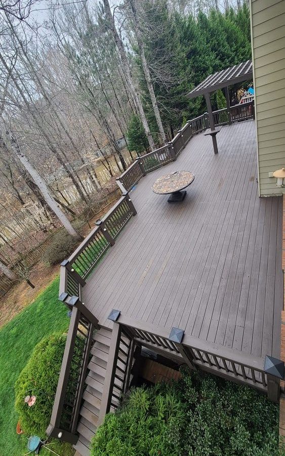 Large stained wood deck with railings and stairs above a wooded lot