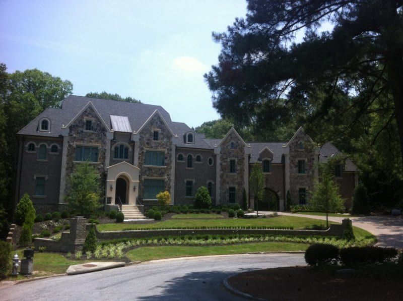 Large stone house with a round driveway and a landscaped lawn