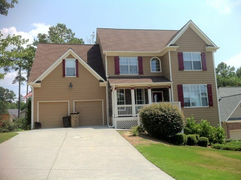 Two-story house with tan siding, red shutters, white porch railings, and two garage doors