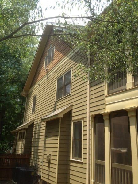 Tan sided house with a covered side porch among trees
