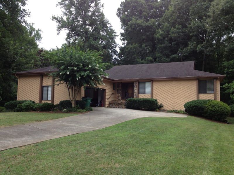 Tan ranch house with a dark roof, a wide lawn, and a curved driveway