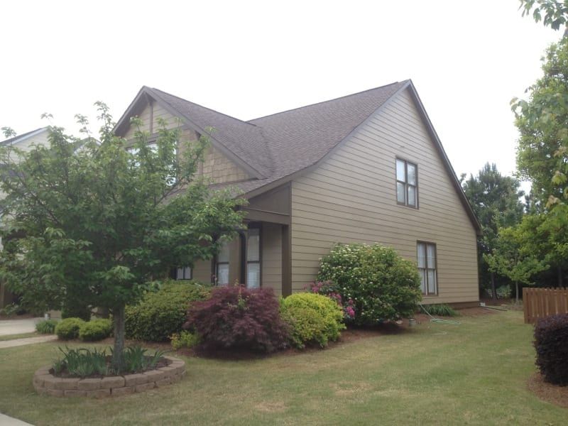 Tan sided house with a dark roof behind a young tree