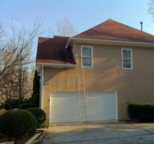 Side of a tan stucco house with a ladder against the wall above the garage