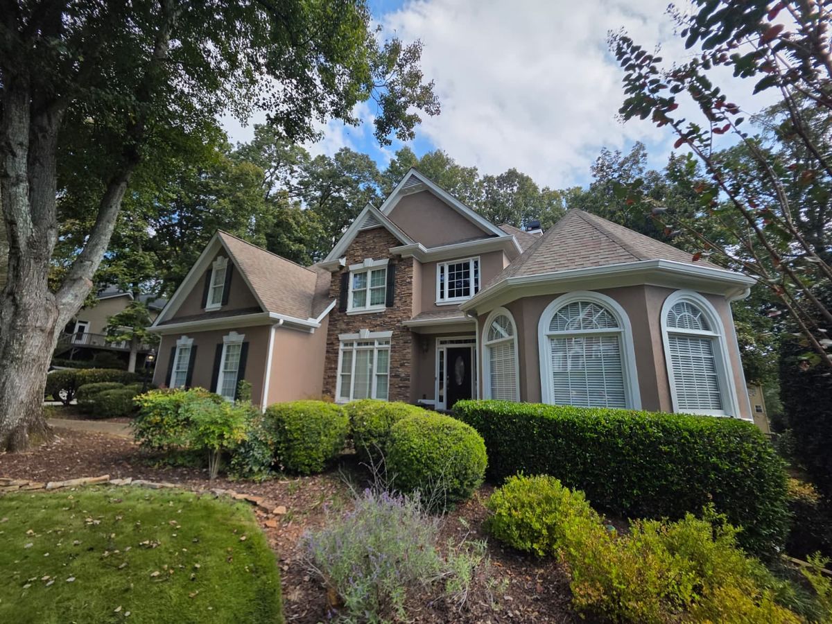Tan stucco two-story house with arched windows behind trimmed shrubs