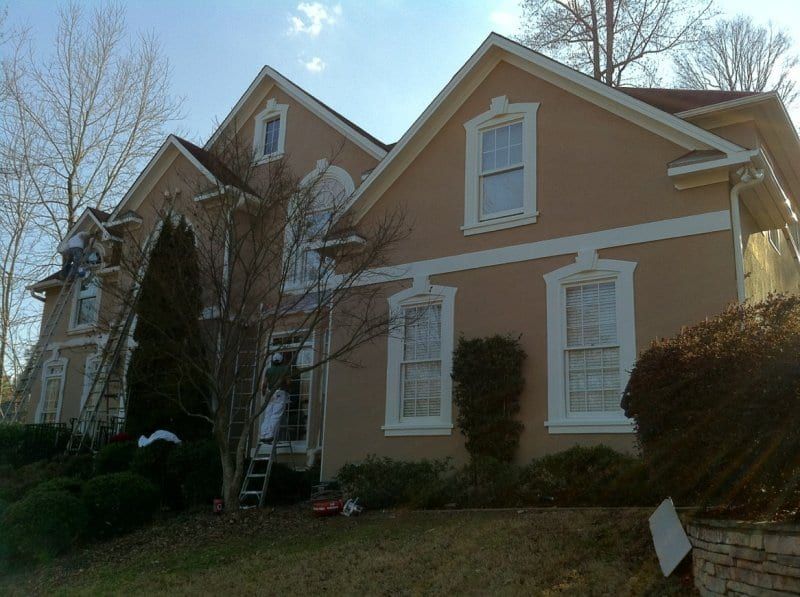Tan two-story house with white trim and ladders at the side