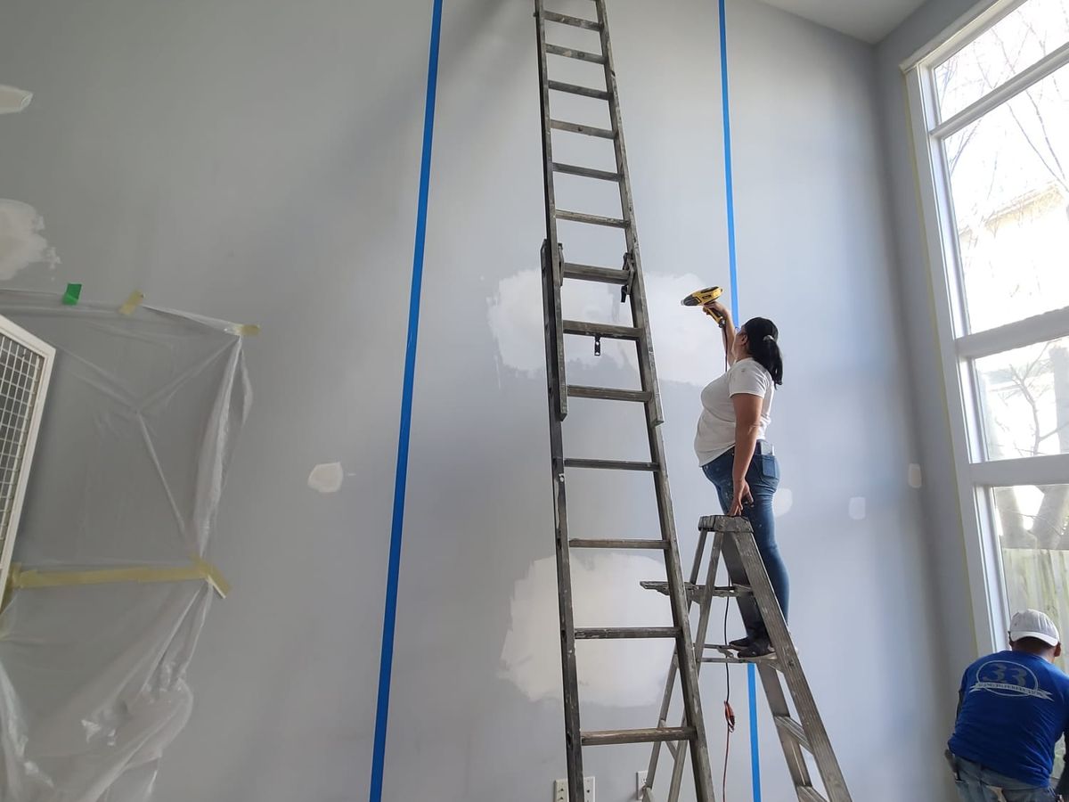 Painters on tall ladders taping off a two-story accent wall