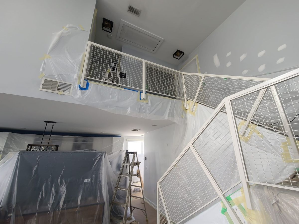 Two-story room covered in plastic, with a metal railing and drywall patches