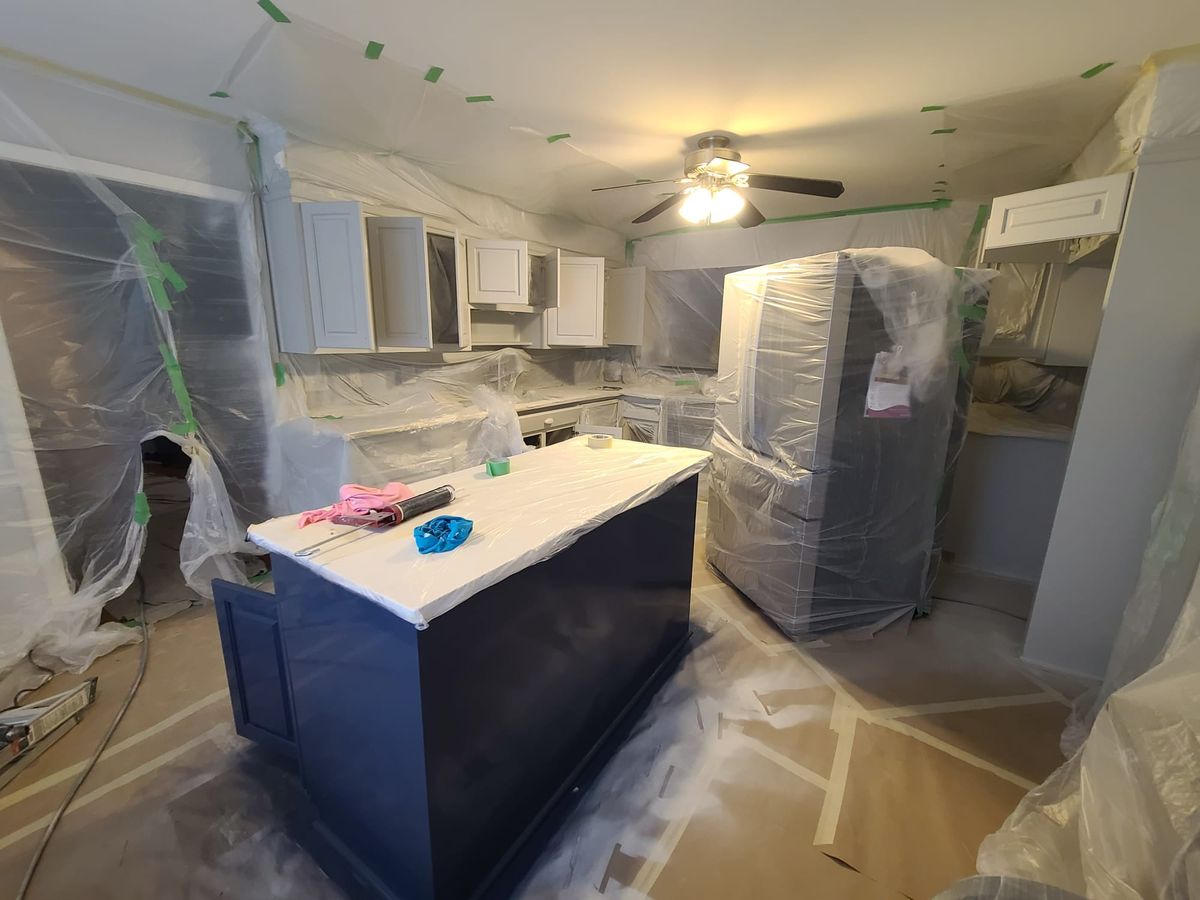 Kitchen covered in plastic sheeting, with the cabinets and island masked for spraying