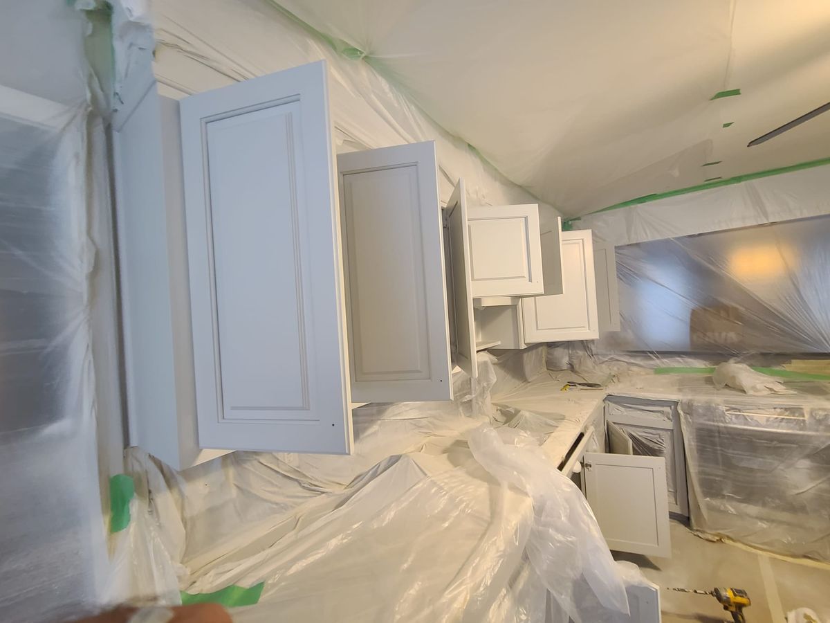 Upper cabinets with their doors open, masked and covered before spraying