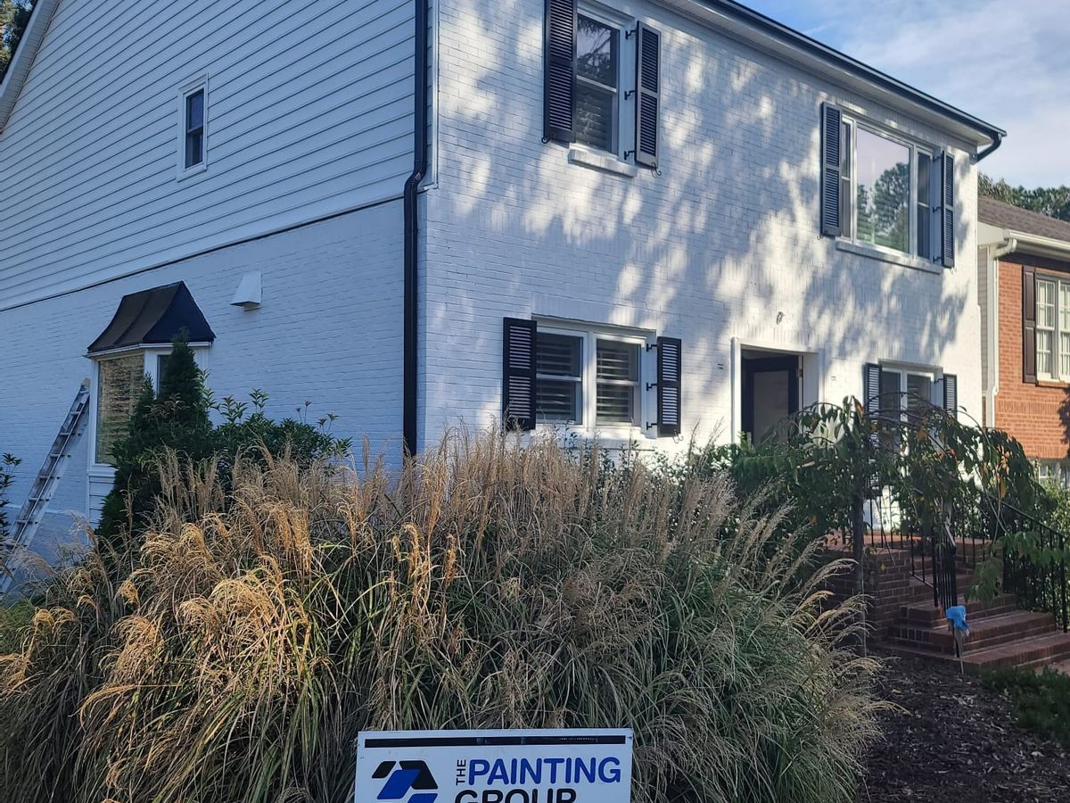 White brick and sided two-story house with black shutters, and our yard sign out front