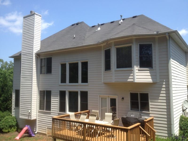 Back of a white sided house with a chimney and a wood deck
