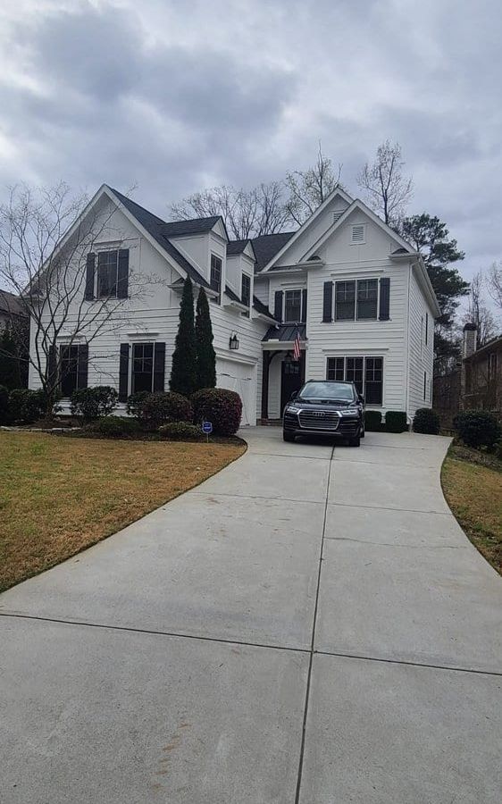 White two-story house with dark trim at the end of a long concrete driveway