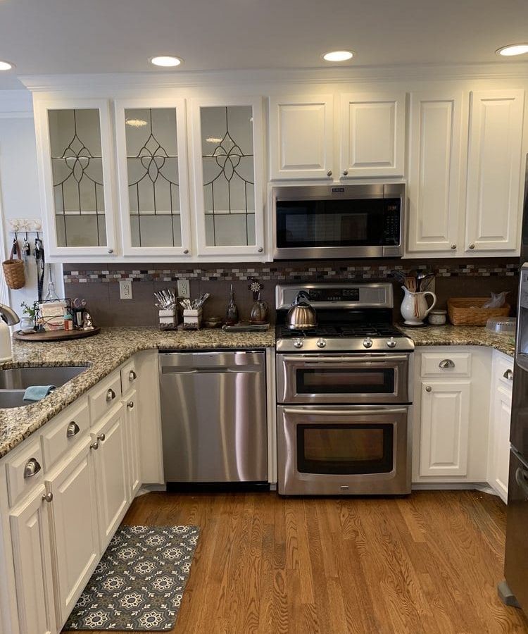 White kitchen with leaded-glass cabinet doors, stainless appliances, and wood floors