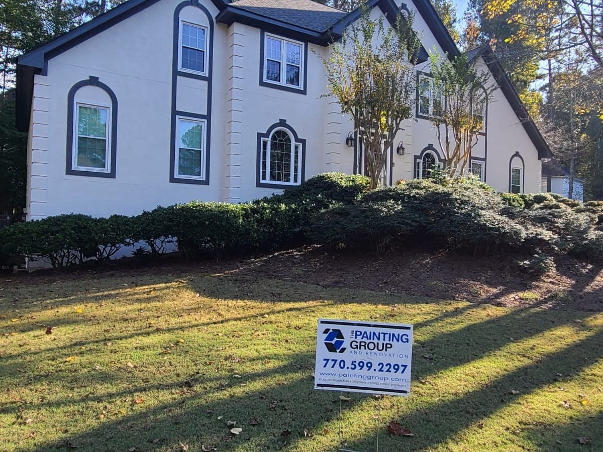 White two-story house with dark trim above a sloping lawn, with our yard sign out front