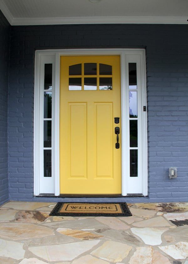 Yellow front door with glass sidelights on a blue-gray brick house
